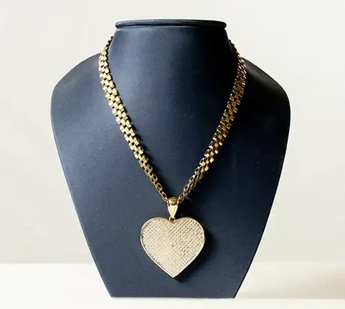Gold chain necklace with a large, diamond-studded heart pendant displayed on a navy blue jewelry bust.