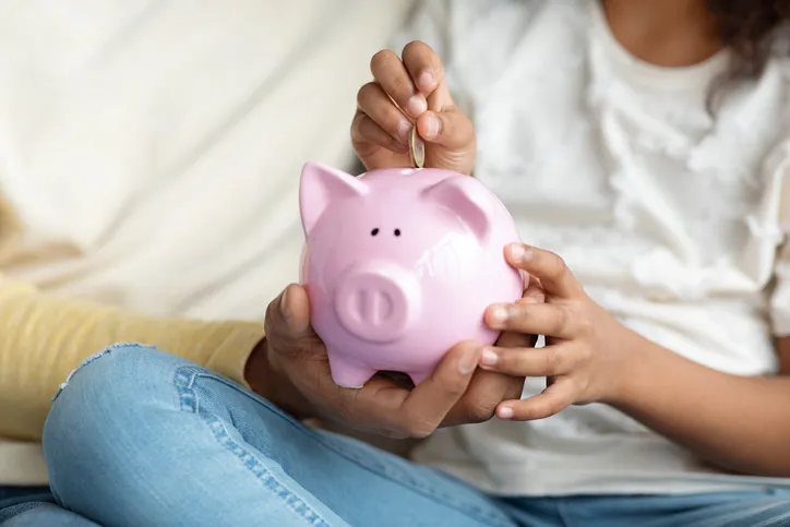 Features a child and an adult holding a pink piggy bank, symbolizing savings and financial education.