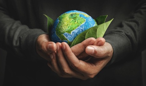 Hands holding a small model of Earth with green leaves, symbolizing environmental protection and sustainability.