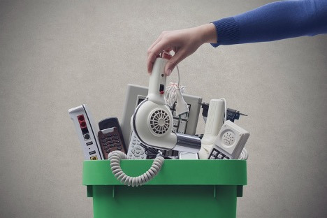 A hand placing electronic devices into a recycling bin, highlighting the importance of recycling electronics to reduce e-waste.