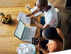 Two people working at a table with documents, a laptop, and a calculator, indicating collaboration or financial planning.